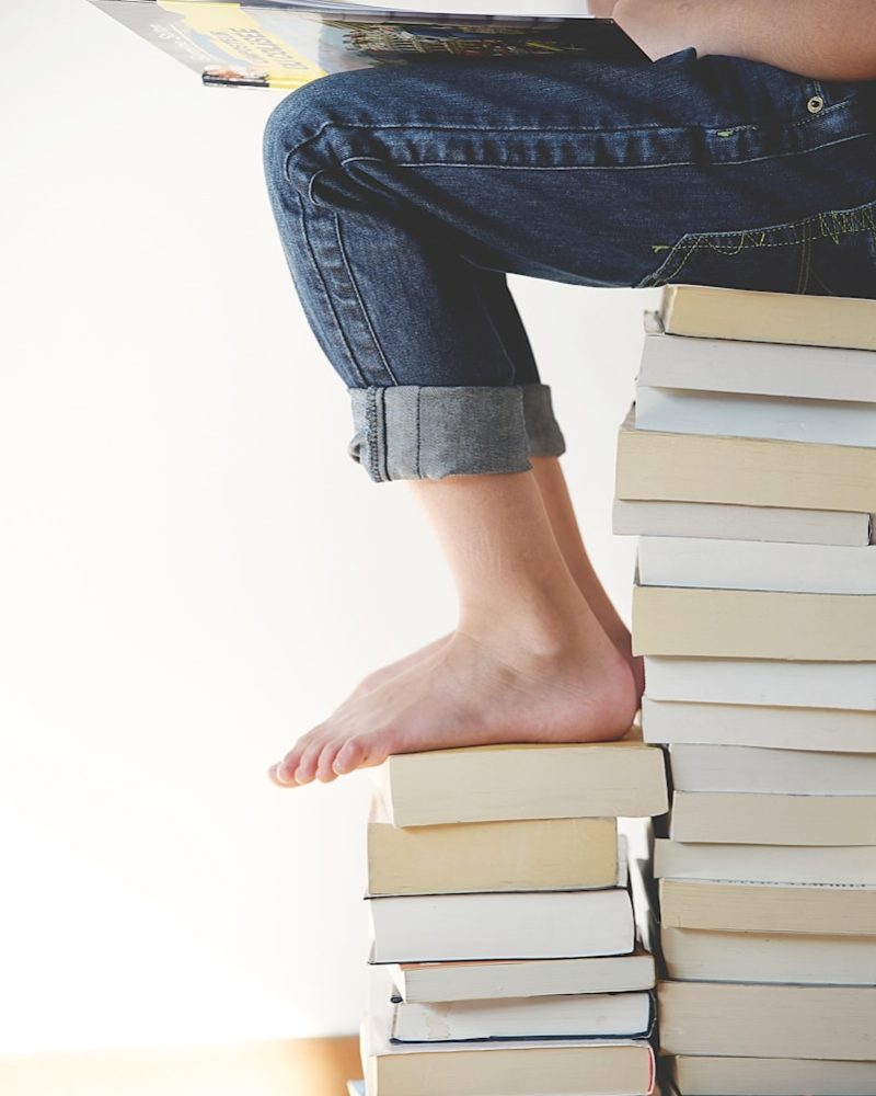 person sitting on stack of books while reading